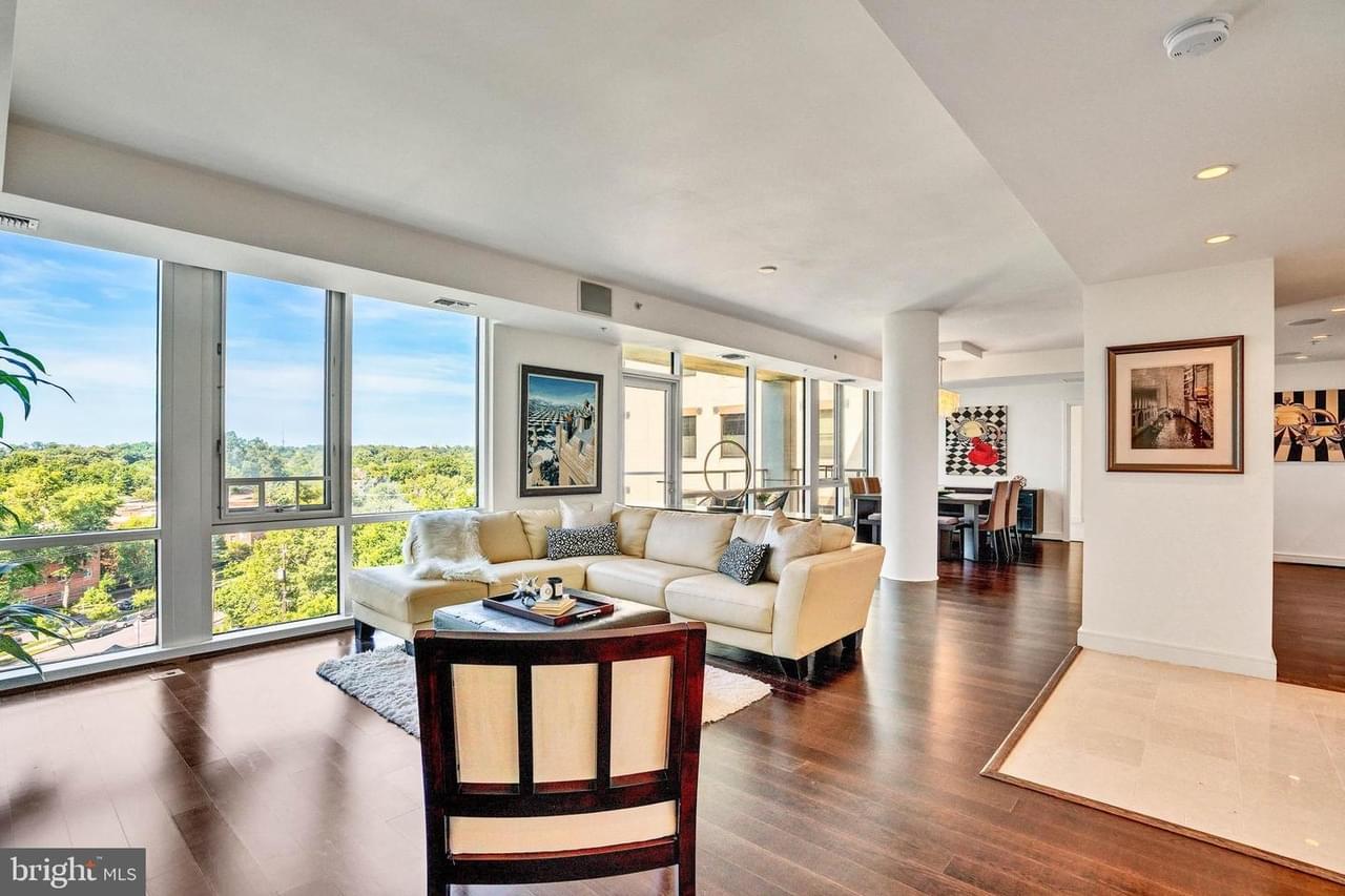 An open concept condo interior with rich wood floor, white walls, floor-to-ceiling windows, and column
